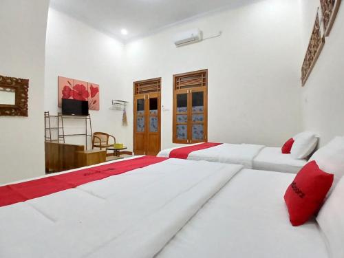 two beds in a white room with red pillows at RedDoorz at Ndalem Eyyang Syariah Stasiun Klaten in Klaten