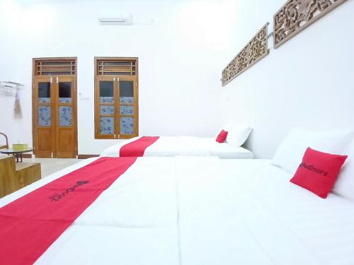 a white bedroom with two beds and red pillows at RedDoorz at Ndalem Eyyang Syariah Stasiun Klaten in Klaten