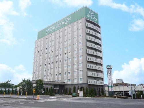 a large white building with a green sign on it at Hotel Route-Inn Hirosaki Joto in Hirosaki