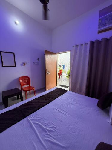 a bedroom with a bed and a door with a chair at Kanak Bihari Yatri Niwas, 100 Meter Ram Ki Paidi, Saryu River in Ayodhya