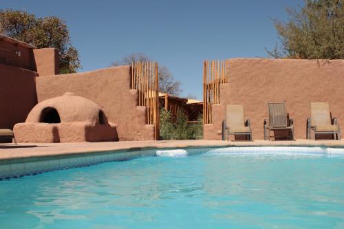 a swimming pool with two chairs and a building at Hotel Poblado Kimal in San Pedro de Atacama
