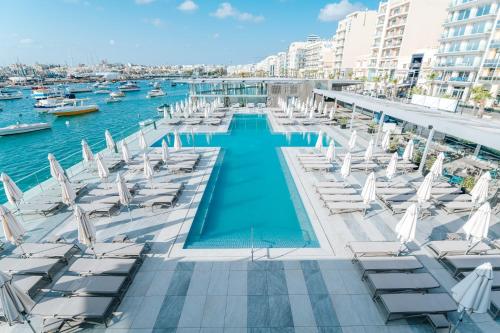 a pool with white chairs and water and buildings at Alavits Hotel by ST Hotels in Il-Gżira
