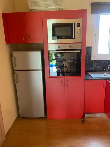 a kitchen with red cabinets and a microwave and a refrigerator at RELAXING POOL HOUSE IN LAGONISI 2 in Kalívia Thorikoú
