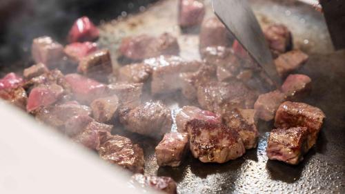 a pile of meat being fried in a pan with a spatula at Motosu Phoenix Hotel in Fujikawaguchiko