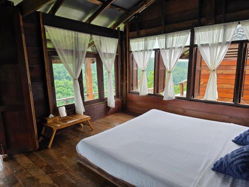 a bedroom with a white bed and windows at บ้านไร่ไอดอย in Phrae