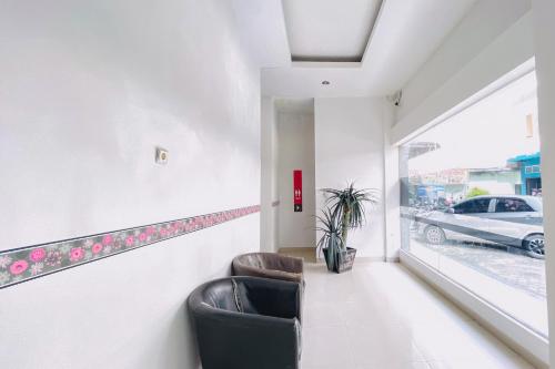 two chairs in a waiting room with a carseen through a window at RedDoorz at STM Suite Medan Amplas in Medan
