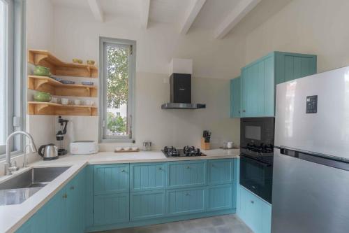 Una cocina con gabinetes azules y un refrigerador blanco. en Villa Mandarina - Luxury 4BHK Villa Near Morjim Beach with Pvt Pool, Pool Table & Kids Playground, en Siolim