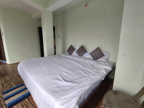 een slaapkamer met een bed met witte lakens en kussens bij Hotel O Sun View in Gangtok