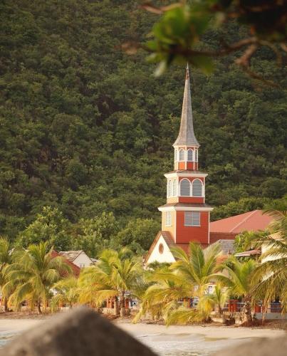 a church with a steeple on a beach with palm trees at KaZandoli in Les Anses-dʼArlets