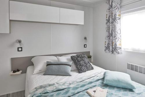 ein weißes Schlafzimmer mit einem Bett mit Kissen und einem Fenster in der Unterkunft Camping de Maillac in Sainte-Nathalène