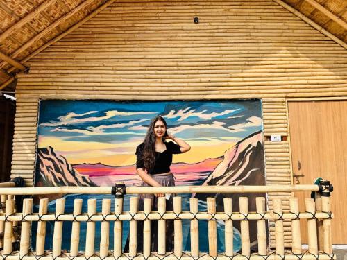 a woman standing on a balcony in front of a mural at Bliss Hampi Eco Resort in Hampi