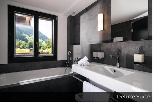 een badkamer met een bad, een wastafel en een raam bij Hotel Arc-en-ciel Gstaad in Gstaad