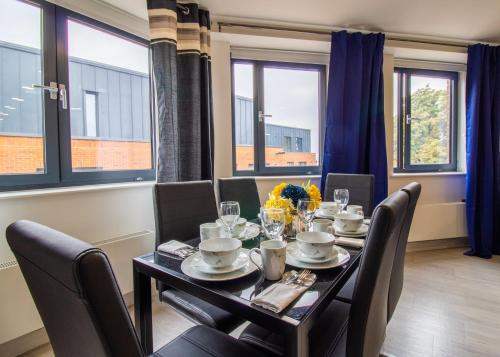 a dining room with a table and chairs and windows at Virexxa Bedford Centre - Alpha Suite - 2Bed Flat with Free Parking & Gym in Bedford