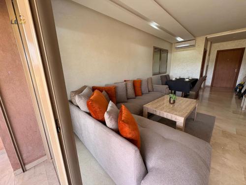 a living room with a gray couch with orange pillows at Appartement Prestigia Agate résidence avec piscine in Marrakech