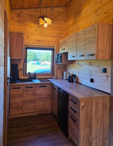 a kitchen with wooden cabinets and a window in a cabin at Domki Pod Olchowym Dachem Lubie in Gudowo