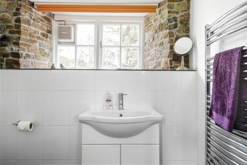 a white bathroom with a sink and a window at Cleave Cottage in Crackington Haven