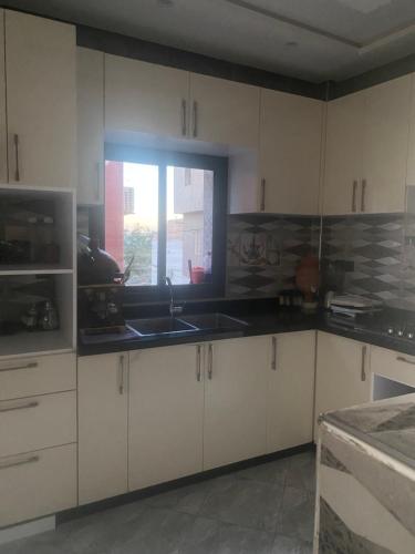 a kitchen with white cabinets and a sink and a window at Appartement complet meublé 2 chambres in Tamraght Ouzdar