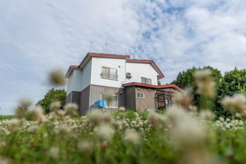 a house is seen behind a field of flowers at 富良野一棟貸しコロポックル in Nakafurano