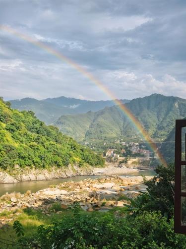 a rainbow over a river with mountains in the background at Waterfront Homestay 2BHK Free Bonfire By Homeyhuts in Mandi