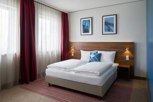 a bedroom with a large white bed with red curtains at Four Points Flex by Sheraton Essen in Essen