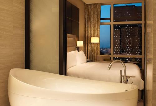 a bathroom with a tub and a bed and a window at Rosewood Abu Dhabi in Abu Dhabi