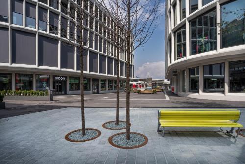 two trees in front of a yellow bench in a city at Solution-Grischun Apartments - Berninaexpress - Städterip - atemberaubende Aussicht in Chur