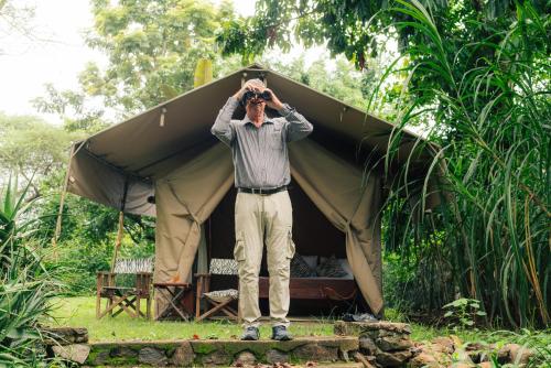 a man is standing in front of a tent at Dolly Farm & River Camp, Luxury Tents in Usa River