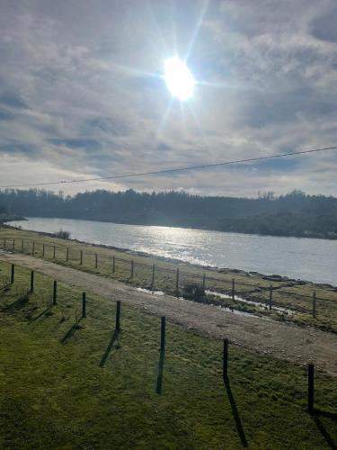 a fence next to a body of water with the sun at Luz de Luna Antilhue in Valdivia