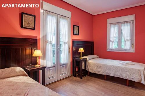 a red bedroom with two beds and two windows at Hotel y Apartamentos La Lonja in Cangas de Onís