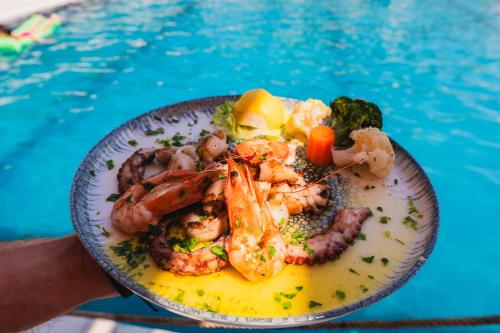 a plate of food with shrimp and vegetables next to a pool at Edva Resort in Vlorë