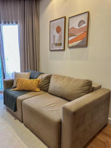 a brown couch in a living room with paintings on the wall at Summit Flat, ótima localização, limpeza diária, academia e piscina in São José dos Campos