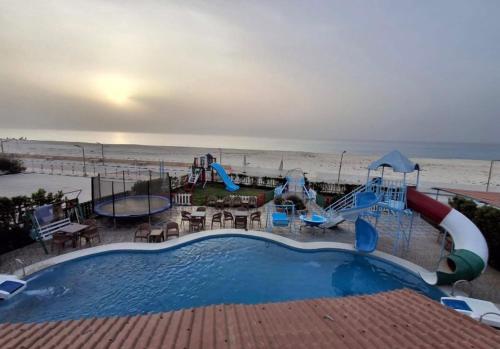 a swimming pool next to a beach with a playground at شالية 180م بالروف 180م قرية هليوبيتش الساحل الشمالي للايجار للعائلات فقط in Dawwār ‘Abd al Qādir Qāsim