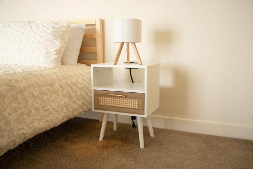 una mesita de noche blanca con una lámpara junto a una cama en Your Home Away from Home, en Corona
