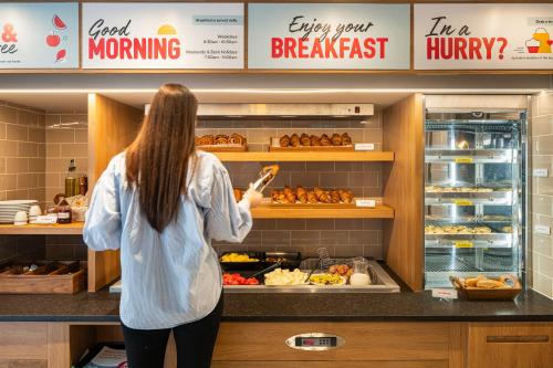 a woman standing at a counter in a bakery at Point A Hotel London Canary Wharf in London