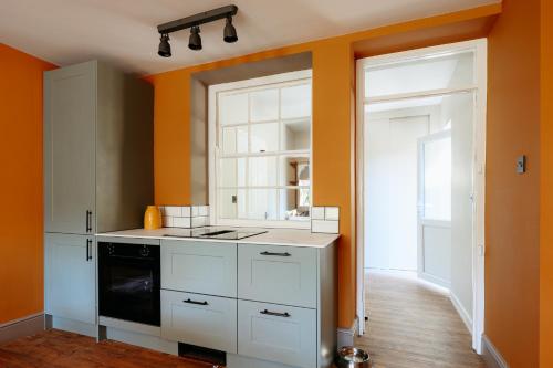 a kitchen with white cabinets and an orange wall at Talfryn Cottages in Betws-y-coed