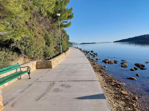 a green bench on a sidewalk next to a body of water at Apartment Rab in Palit