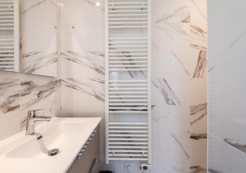 a bathroom with white marble walls and a sink and mirror at L'Apparté Confort in Thonon-les-Bains