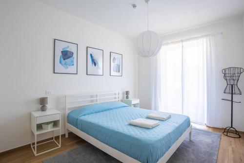 a white bedroom with a blue bed and a window at The Window on the Lake - Balcony Beaches Playground in Brusimpiano