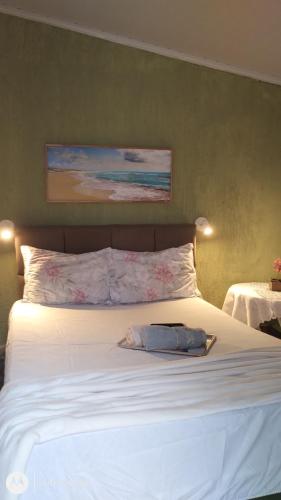 a bedroom with a bed with white sheets and a painting at Minicasa climatizada - Volta Redonda in Volta Redonda