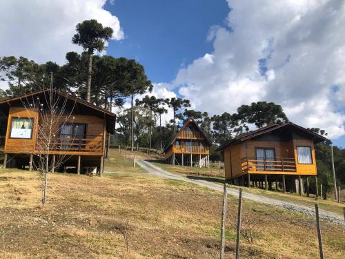 a group of three wooden cabins in a field at Hospedagem Família Cruz in Urubici