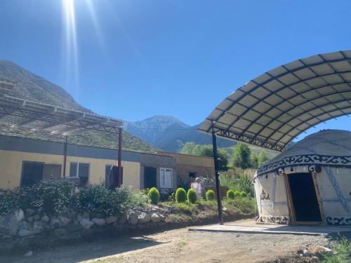 a building with a shelter with a mountain in the background at Taldy-Bulak Guest House in Barskoon
