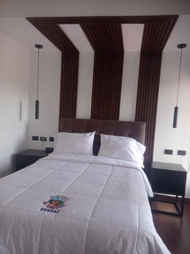 a bedroom with a large white bed with a wooden headboard at Hotel El Castor in Huaraz