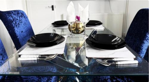 a glass table with chairs and a glass table with plates and glasses at Modern Haven in Luton