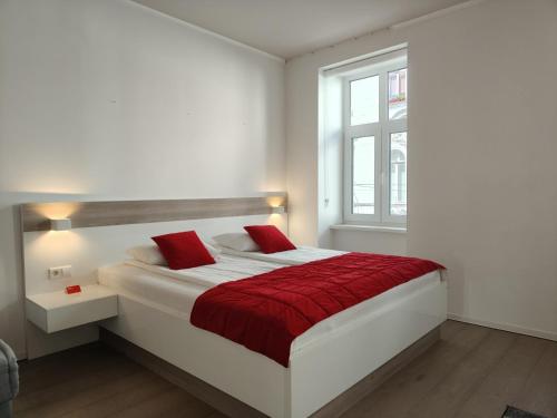 a white bedroom with a bed with red sheets and a window at Central Point Privilege Apartments in Sarajevo