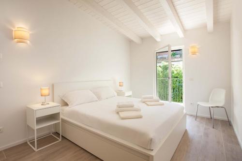 a white bedroom with a white bed and a window at Modern Apartment with Lake View in Castelletto di Brenzone