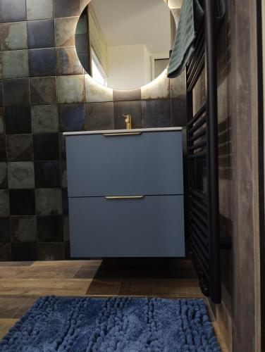 La salle de bains est pourvue d'un lavabo, d'un miroir et d'un tapis bleu. dans l'établissement Les Chambres des Ardillers, à Saint-Pierre-le-Vieux