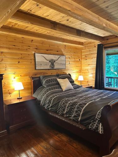 Un dormitorio con una cama en una cabaña de troncos en Le repère de la Rivière, en Saint-Alexis-des-Monts