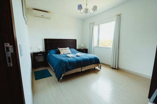 a bedroom with a bed with a blue comforter and a window at Casa Pampa Cabañas in Chapadmalal