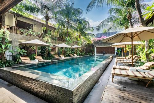 a swimming pool with lounge chairs and umbrellas at Kejora Suites in Sanur