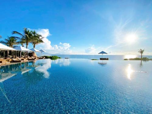 a swimming pool with chairs and umbrellas and the ocean at Fusion Resort Cam Ranh - All Spa Inclusive in Cam Ranh